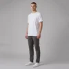 Man standing wearing a plain white t-shirt, dark gray trousers, and white sneakers against a gray background