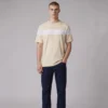 Man wearing a beige crewneck t-shirt with a white horizontal chest stripe and dark blue jeans